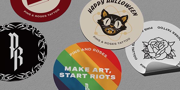 Various circular stickers featuring designs from Pins & Roses Tattoo, including a Halloween theme and rainbow colors.