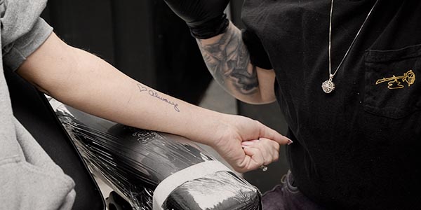 A tattoo artist prepares to tattoo a client's arm, which has a design sketched on it.