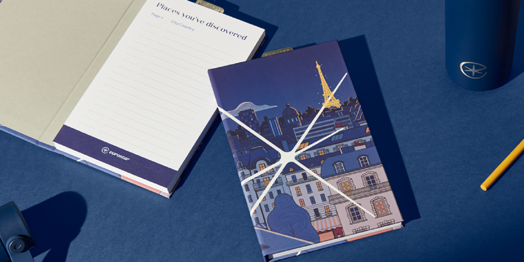 A colorful notebook featuring Parisian skyline and Eiffel Tower, alongside a notepad, pen, and water bottle.