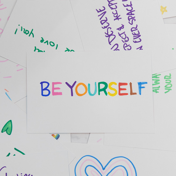 Colorful card reads "BE YOURSELF," surrounded by handwritten notes and drawings.