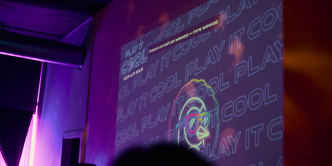 Colorful wall projection displays text and a cartoon bird with sunglasses at a pop-up bar event.