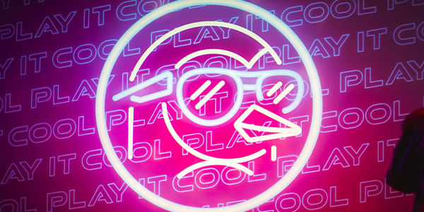 Neon sign of a penguin wearing sunglasses with "PLAY IT COOL" text in the background.