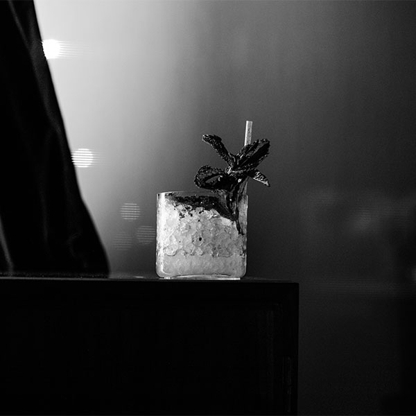 A glass of cocktail with ice and a decorative garnish sits on a dark surface.